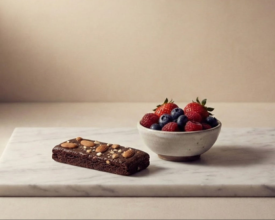 That's all protein bar with nuts next to a bowl of berries on a marble surface